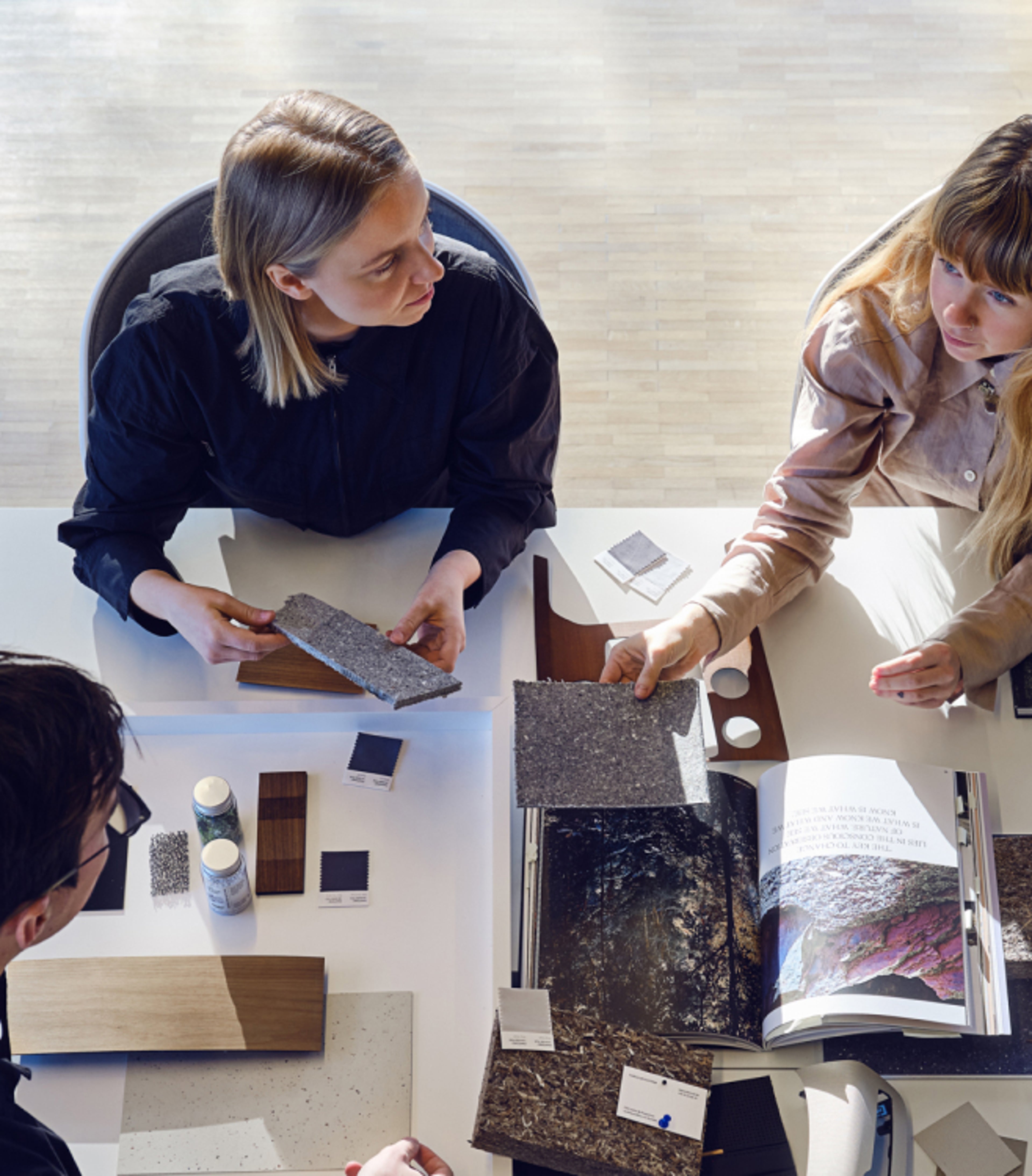 两名女士和一名男士围坐桌旁讨论材料。