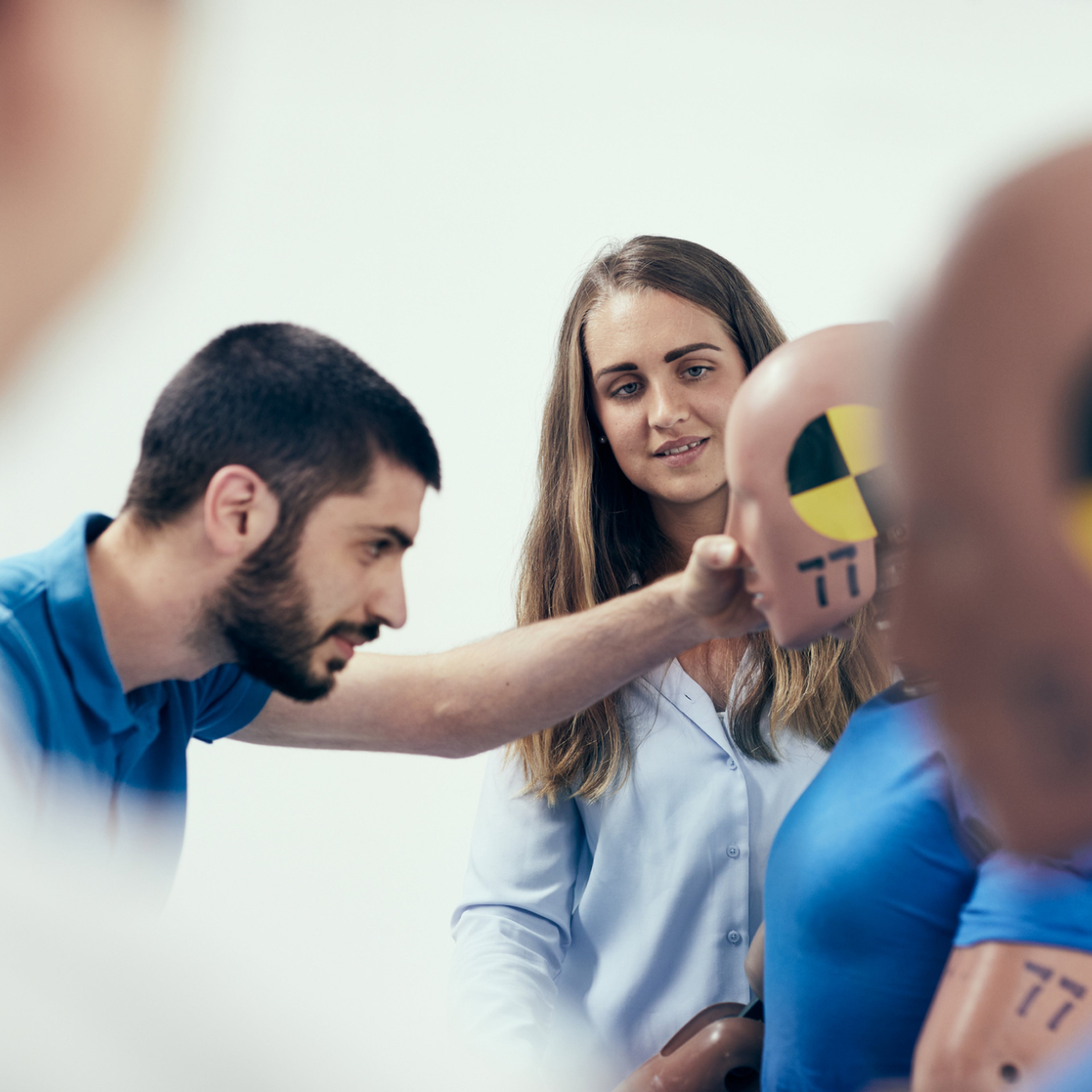 一名男士正在检查碰撞测试假人,另一名女士在旁观察。