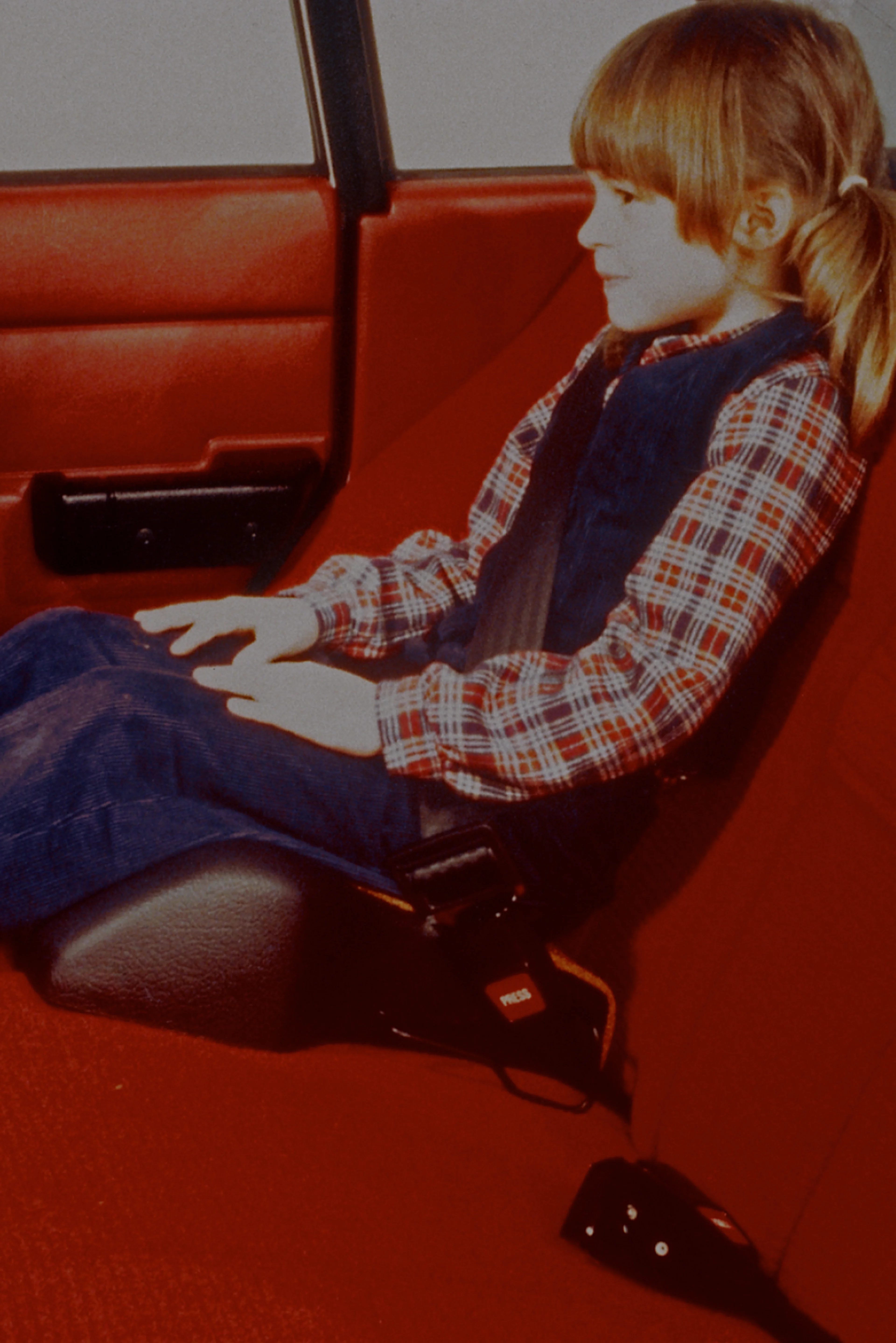 一个女孩系着安全带,坐在一辆红色内饰沃尔沃汽车的增高座椅上。