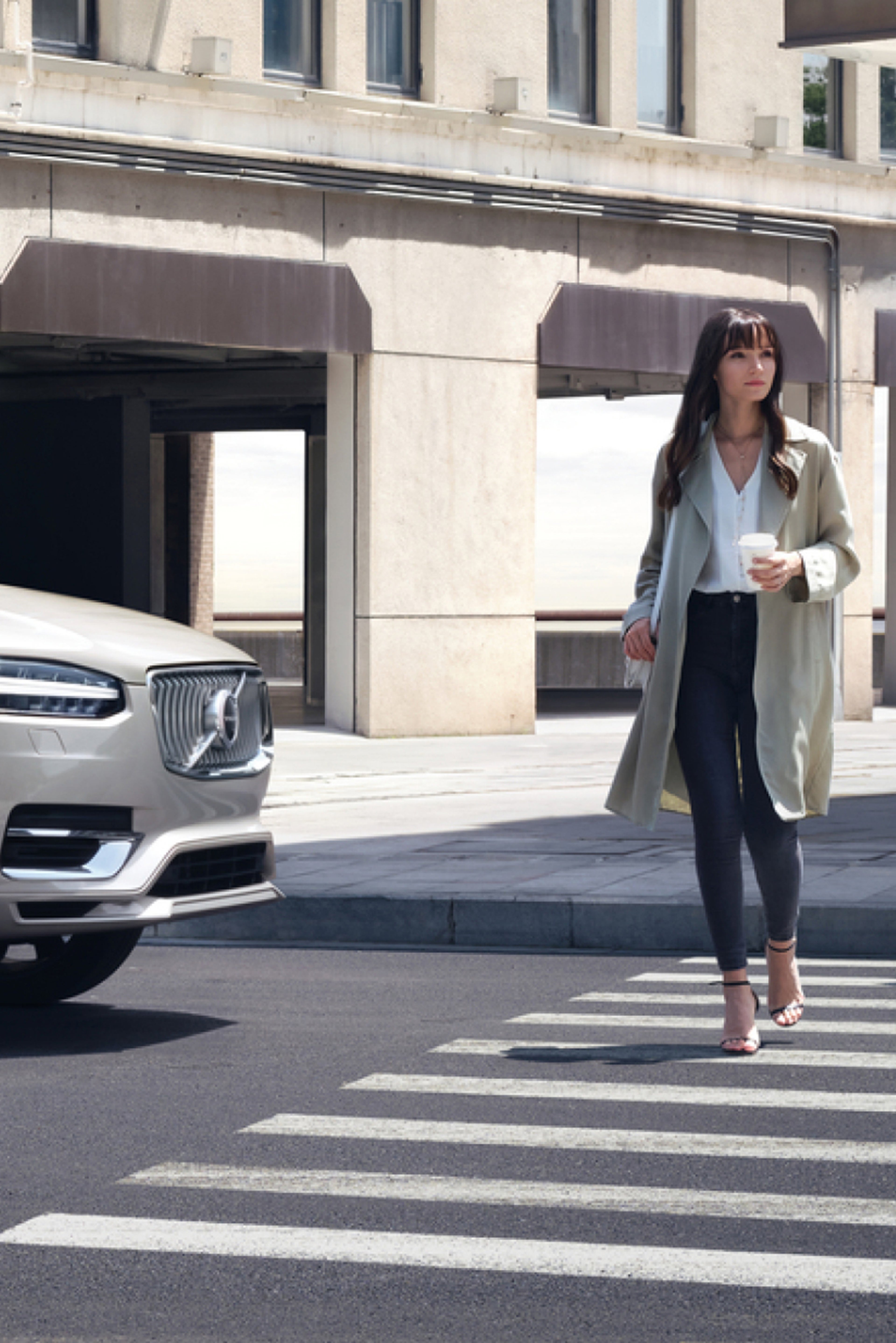 一辆 VOLVO XC90 停人行道前,等候手握咖啡杯的女士穿过。