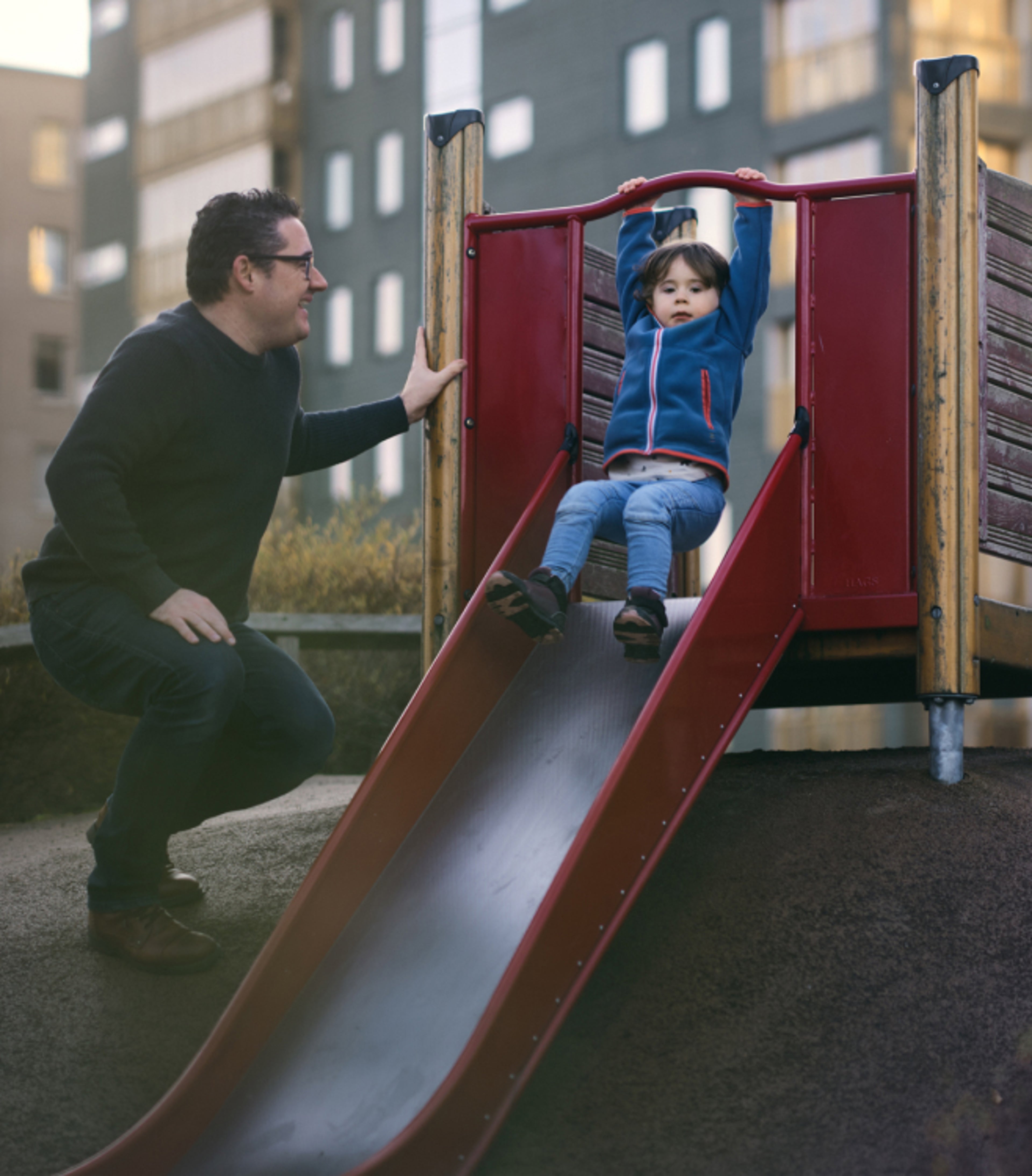 儿童游乐区内,一名男士微笑着望着从滑梯上下来的幼儿。