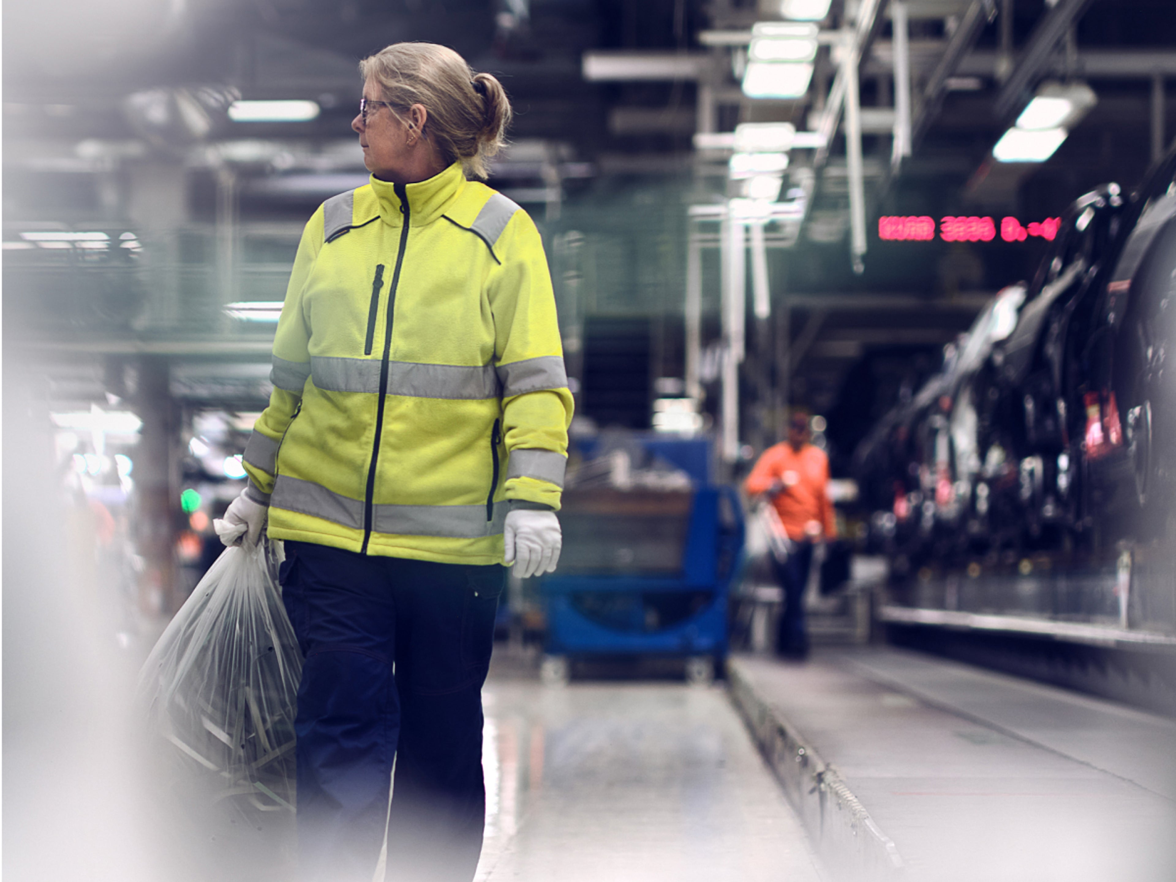 穿工作服女士拎着塑料袋望向右边。