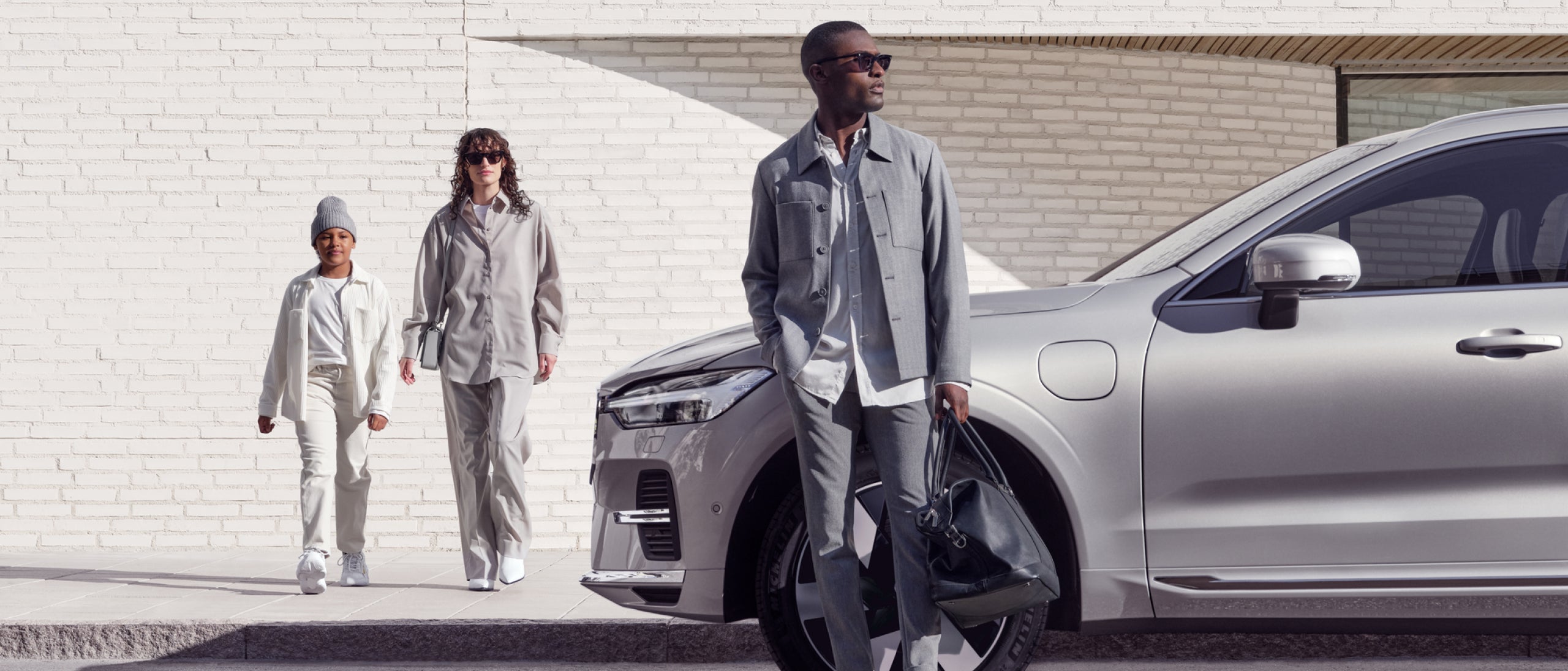 男子倚靠沃尔沃车旁,左边有 2 名行人。