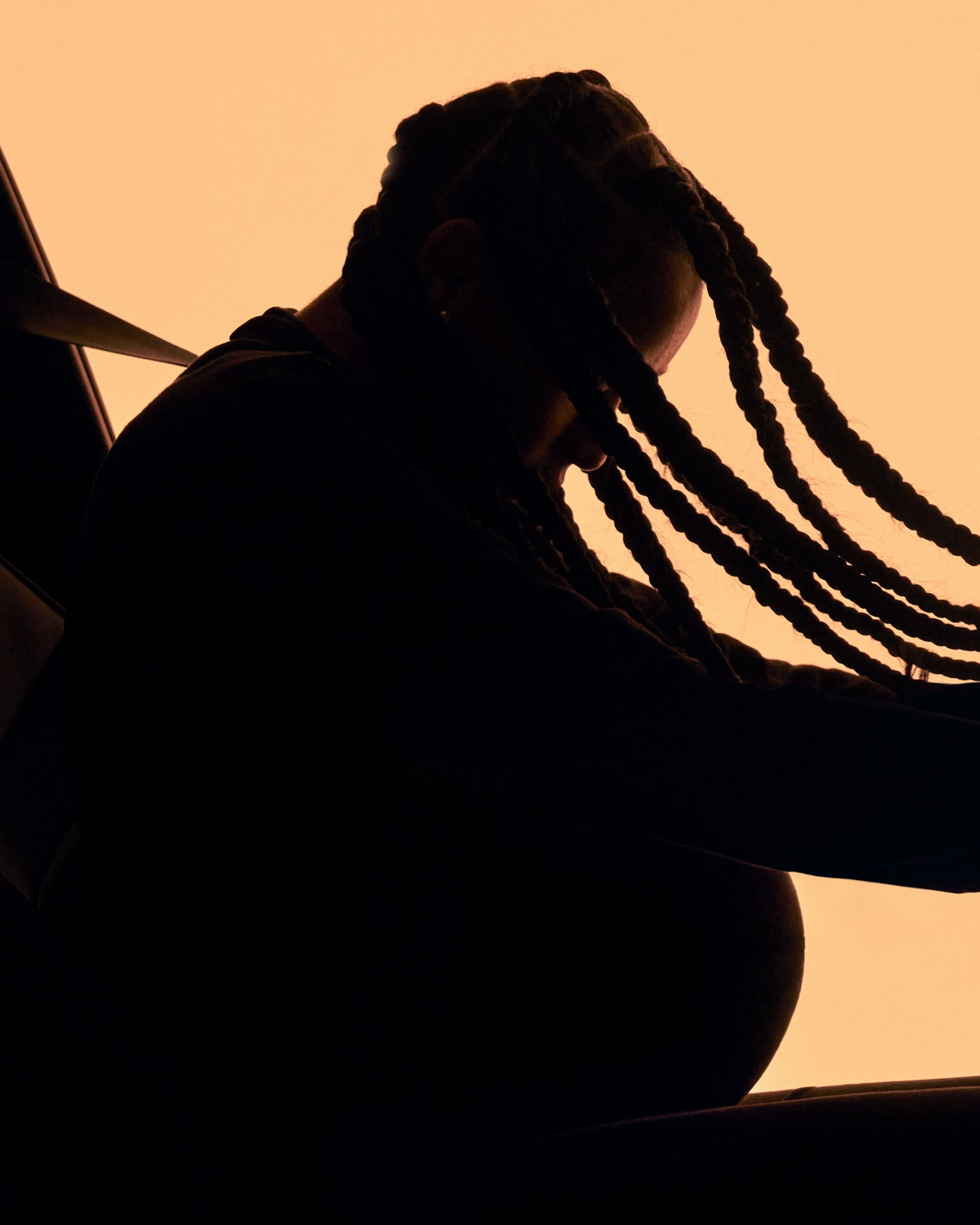 梳着辫子的侧影孕妇,俯身坐于车内座椅,展示多方位自适应安全带。