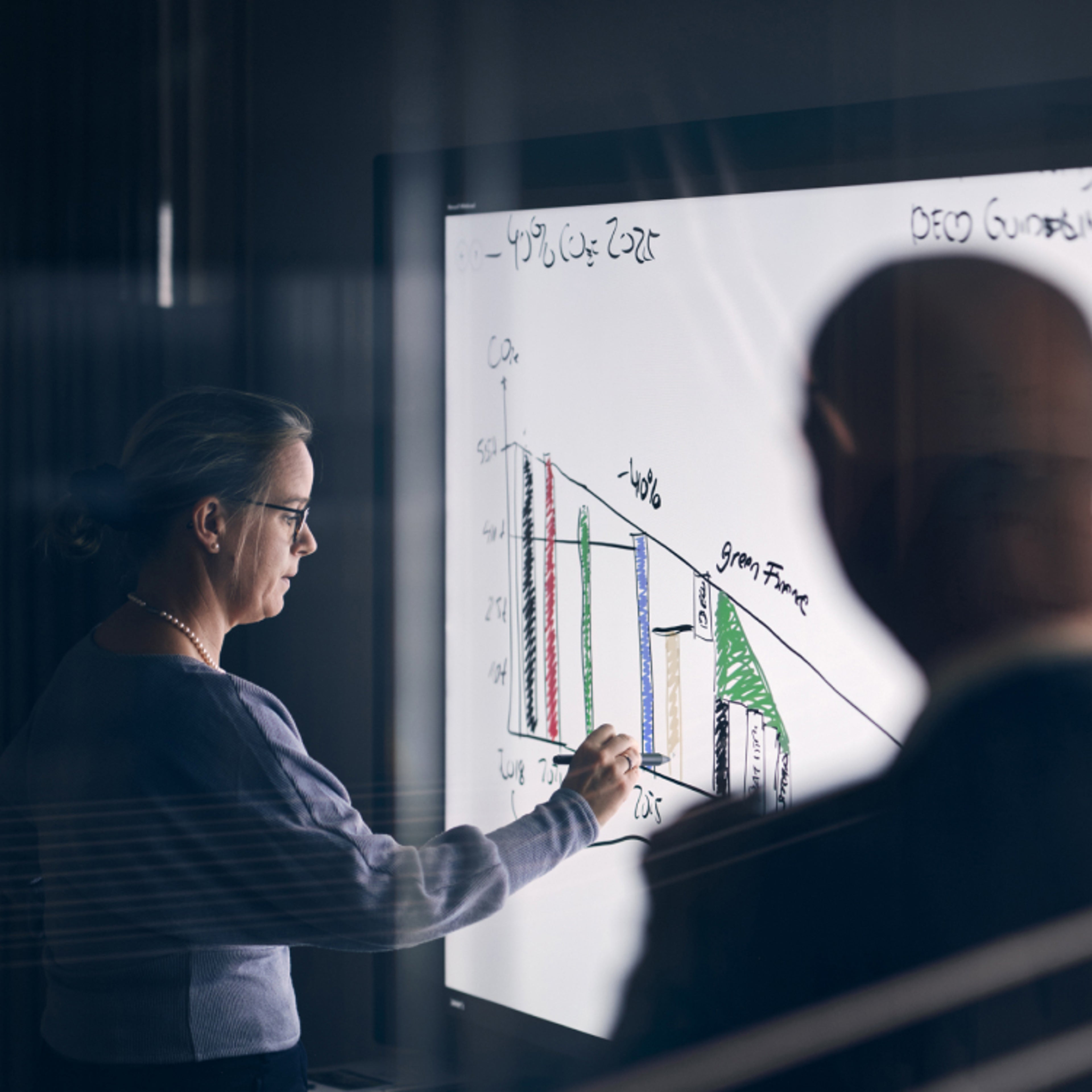 一名男士在观察着一名手握触摸笔在智能平板上工作的女士。