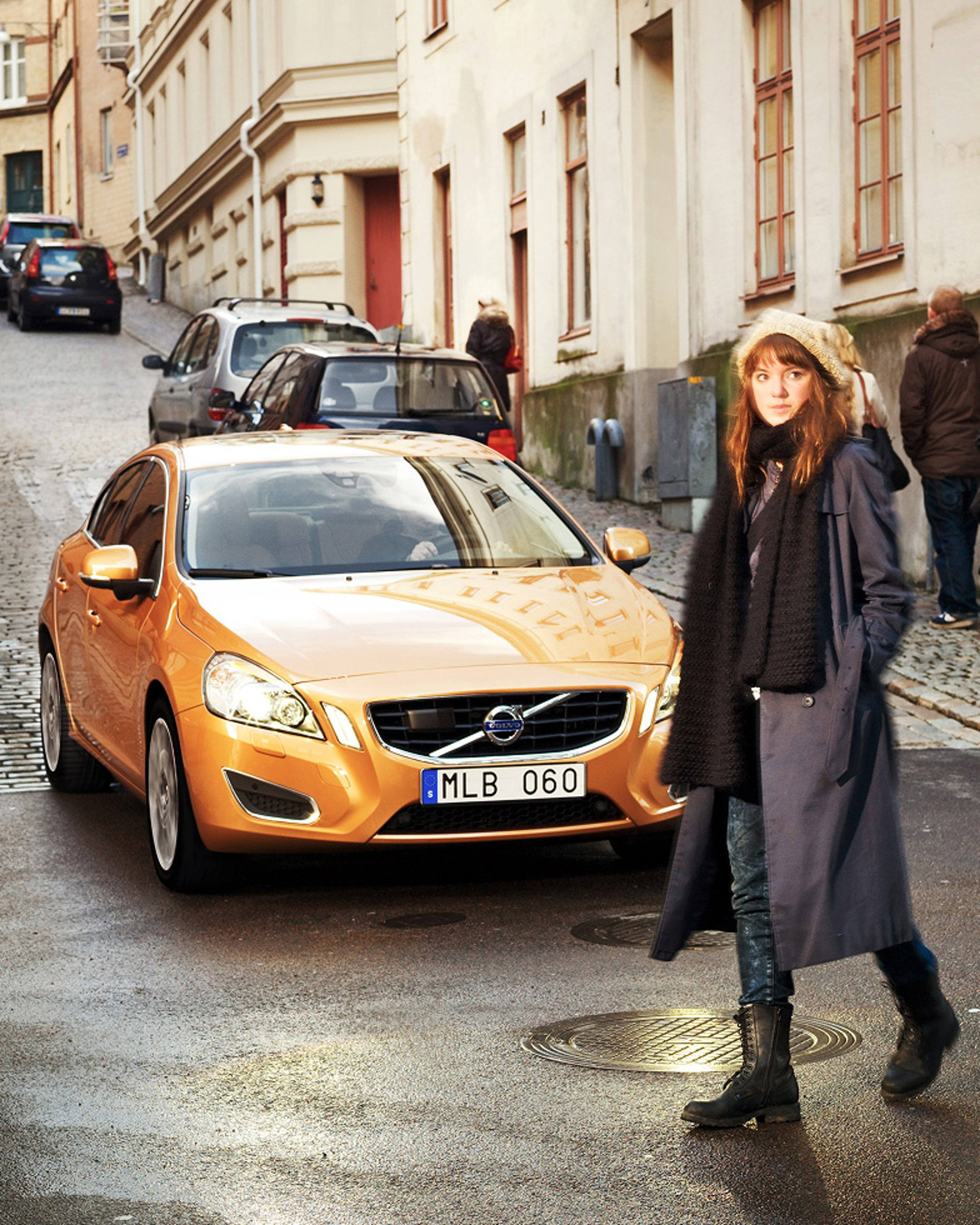 一辆橙色的沃尔沃汽车停在一条小路上,一名女子在车前行走。