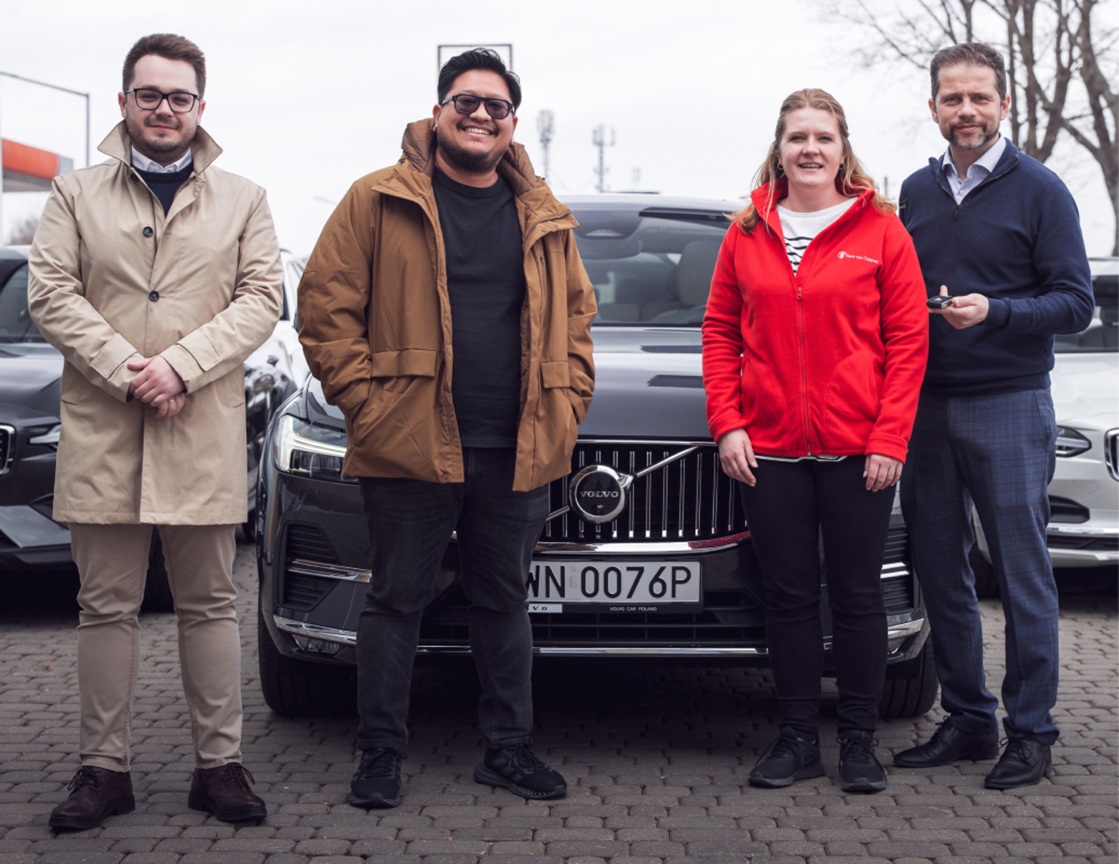 三名沃尔沃汽车员工站在三辆沃尔沃汽车前,将车钥匙交给一位来自救助儿童会(Save the Children)的妇女。