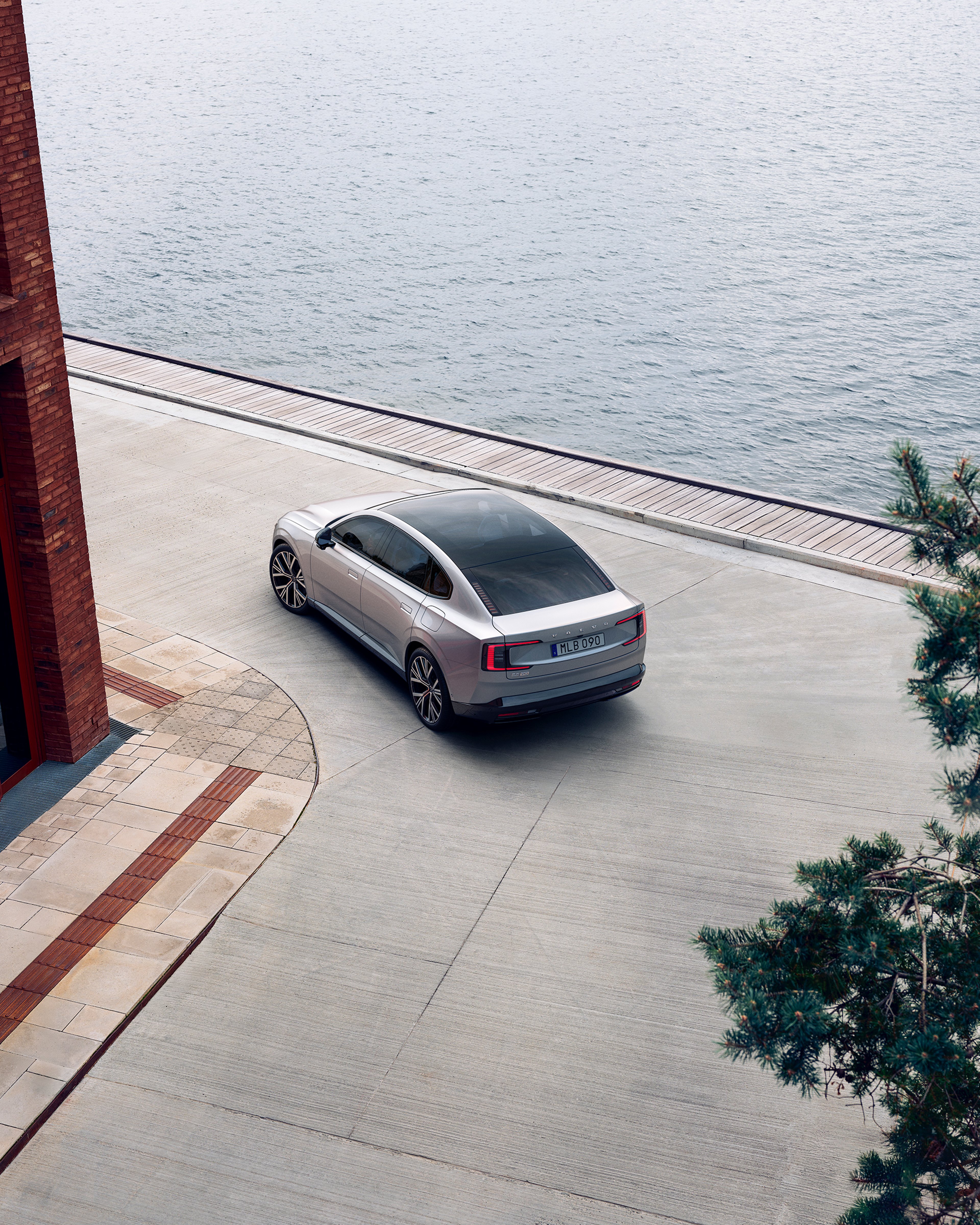 沃尔沃 ES90 车尾视角,行驶于滨水区域砖楼附近。