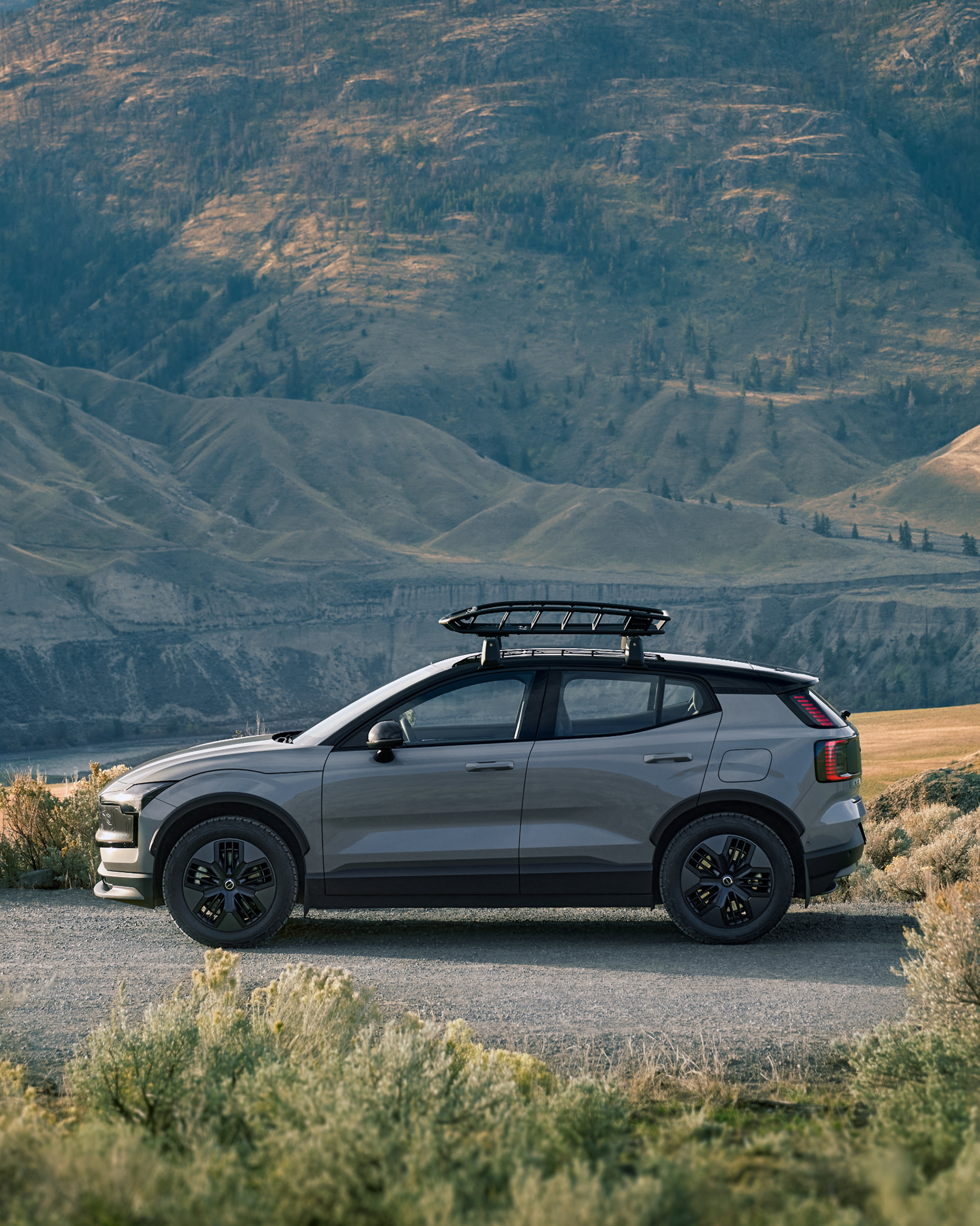 EX30 Cross Country 带着车顶框在丘陵中行驶的侧面图。