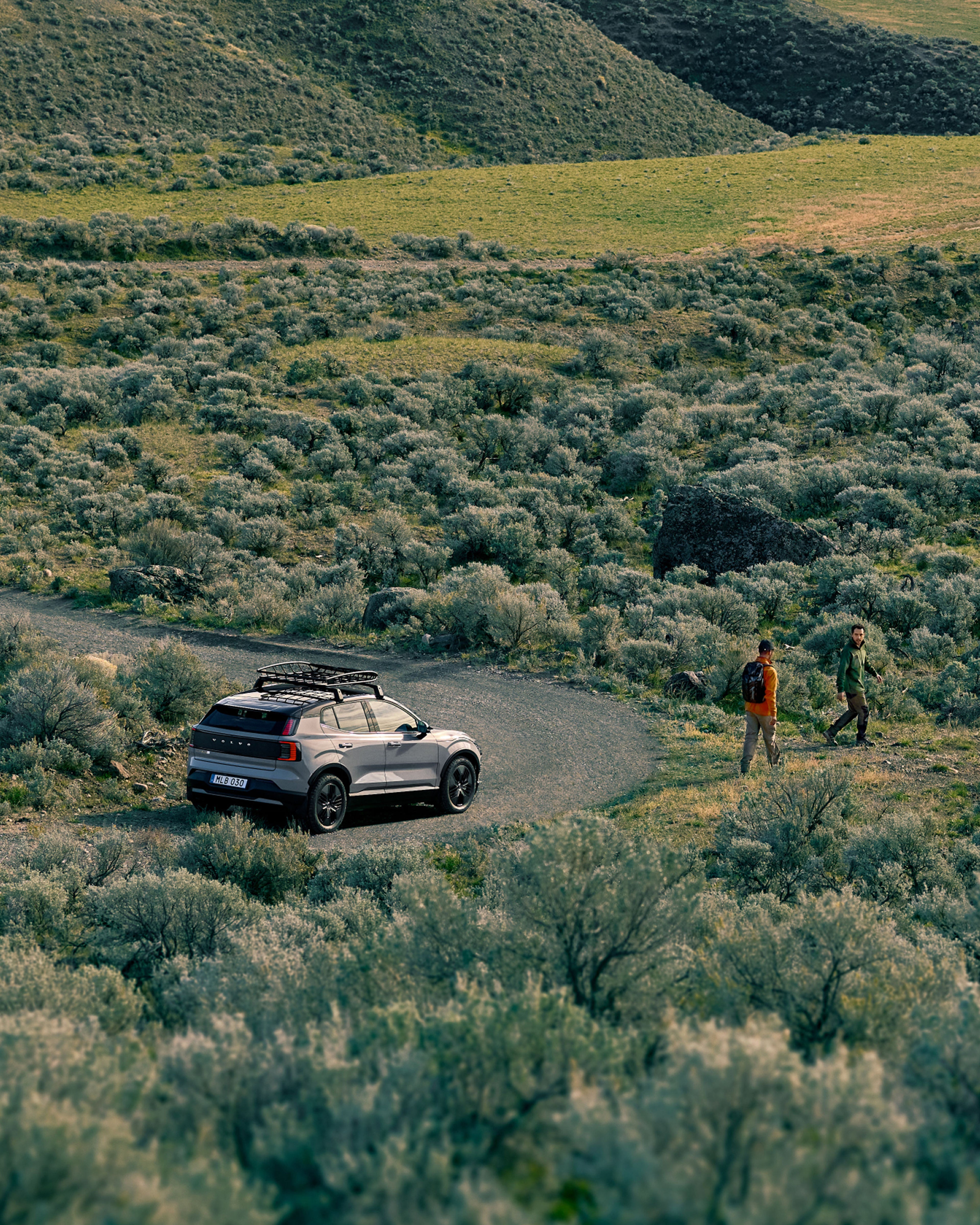 EX30 Cross Country 装备了车顶行李架,停在草地上,两名男子正在徒步。