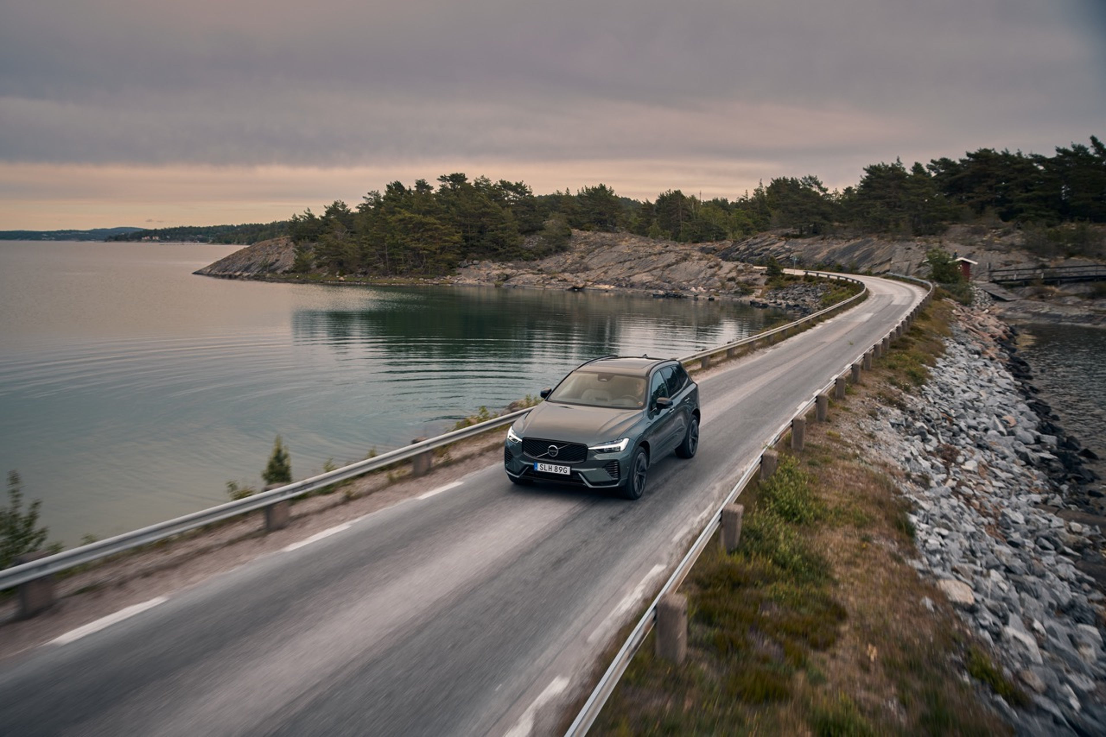灰色沃尔沃 XC60 行驶在日落时分瑞典海岸线旁的道路上。