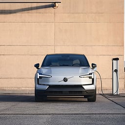 一辆电动Volvo车在晴天的停车场公共充电站插电的正面视图。