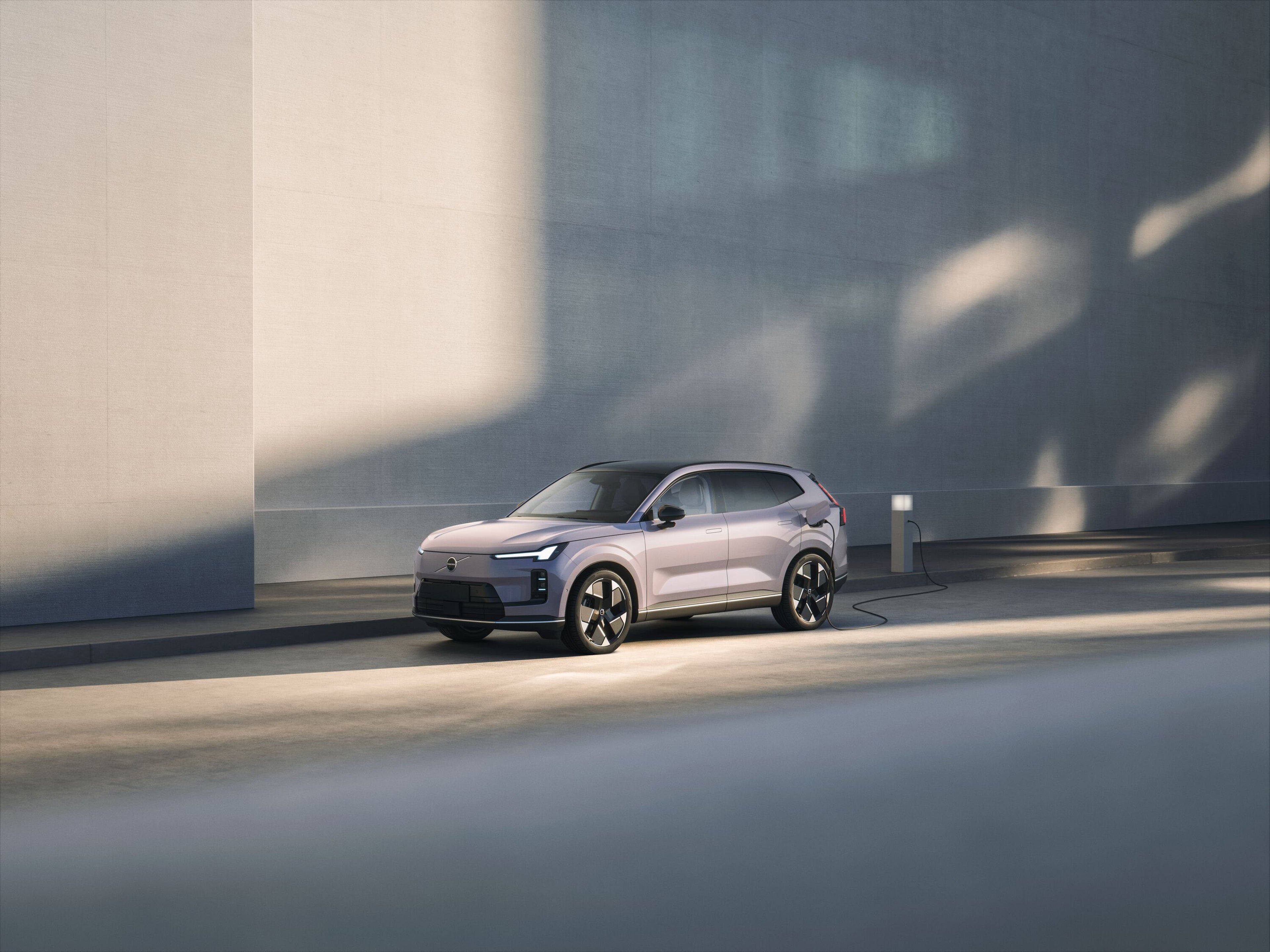 一辆沃尔沃 XC70停在阳光明媚的街道上,与高大的混凝土墙旁的充电站相连。