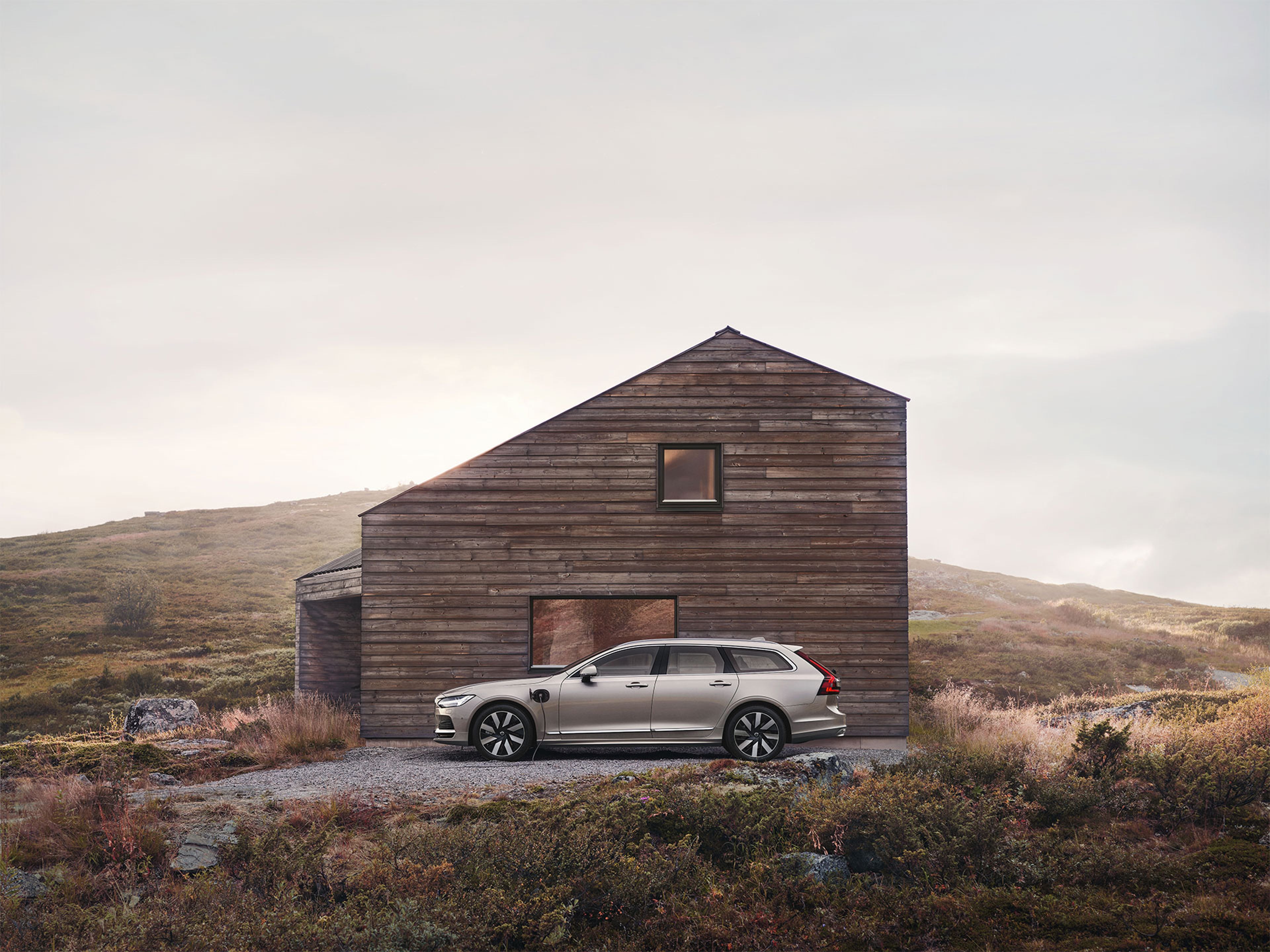 V90 插电式混合动力汽车在斯堪的纳维亚荒野小屋外停车充电时侧面轮廓。