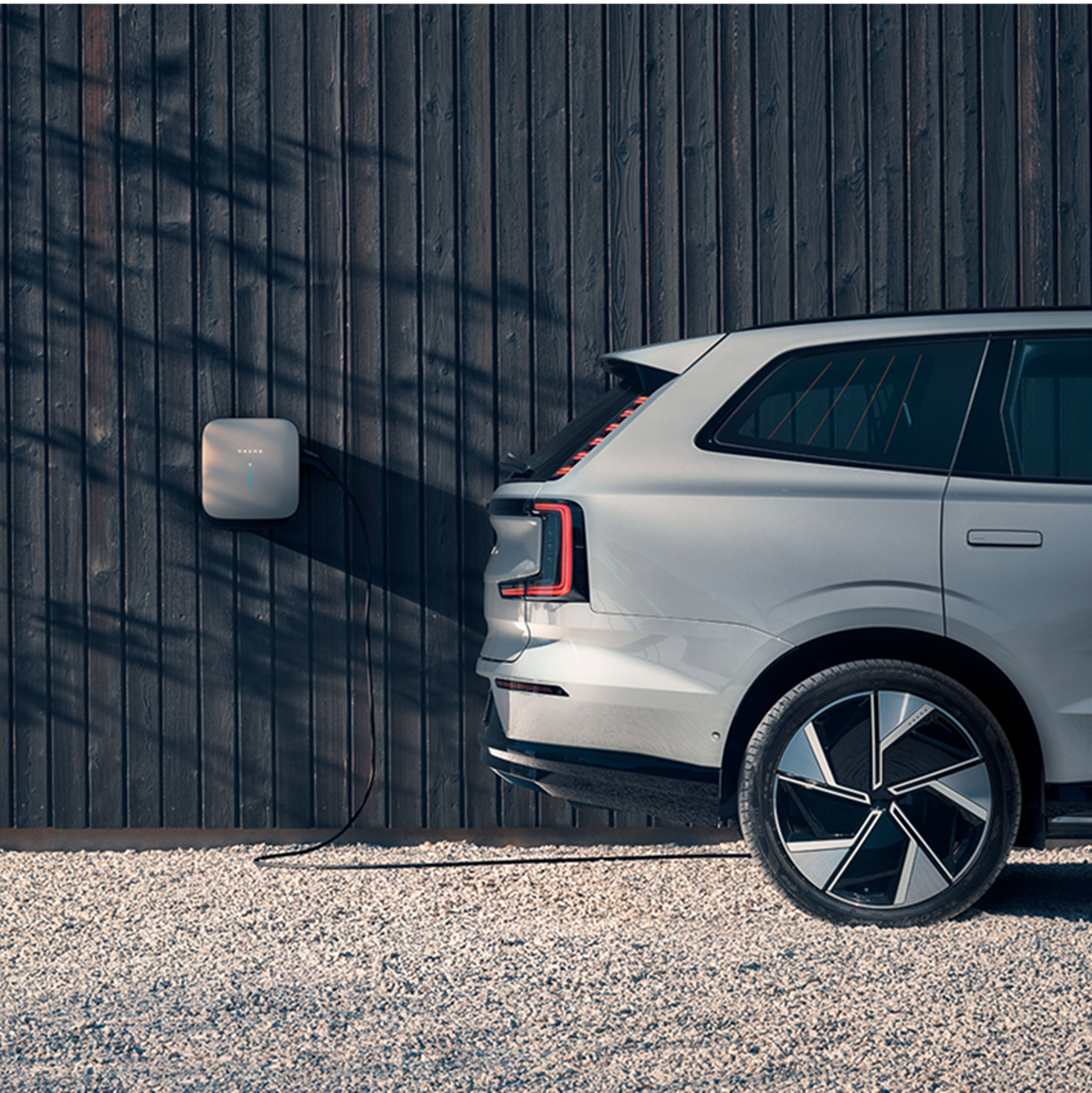白色沃尔沃 SUV 靠着木质外墙的壁挂式充电器充电。