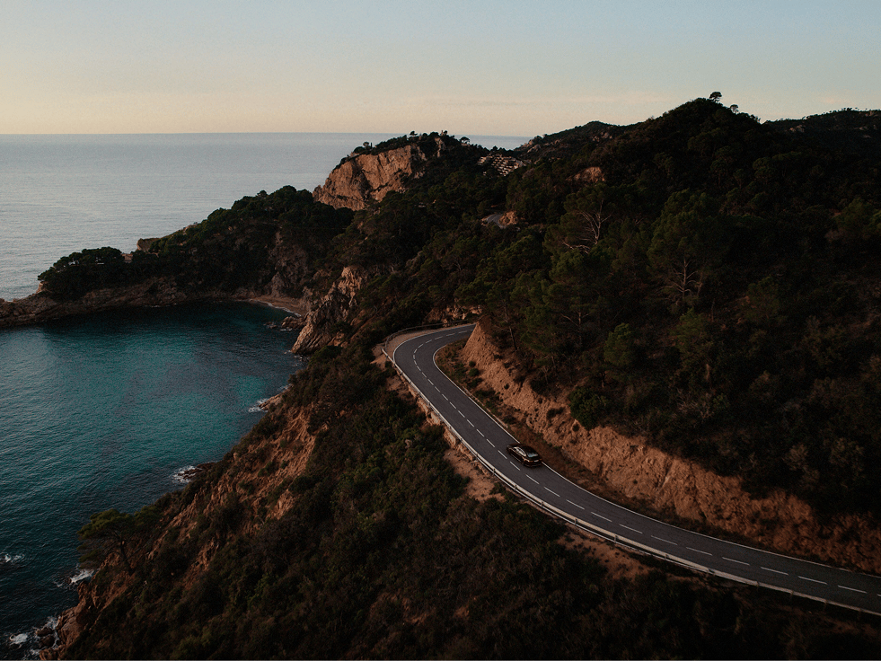 一辆沃尔沃电动汽车在悬崖峭壁和森林环绕的蜿蜒沿海公路上行驶。