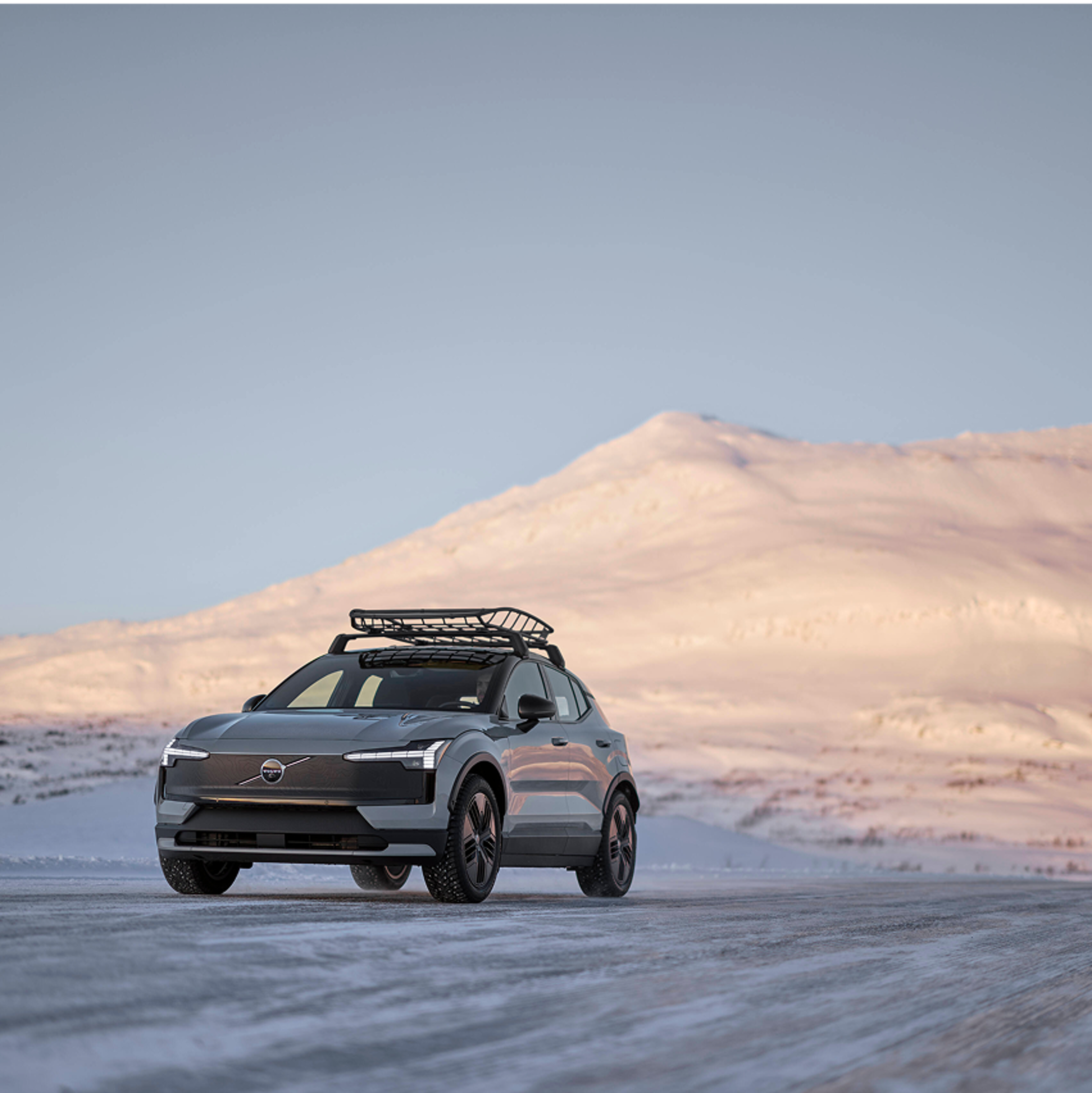配备车顶行李架的沃尔沃 EX30 在阳光普照的群山背景下行驶在白雪皑皑的道路上。