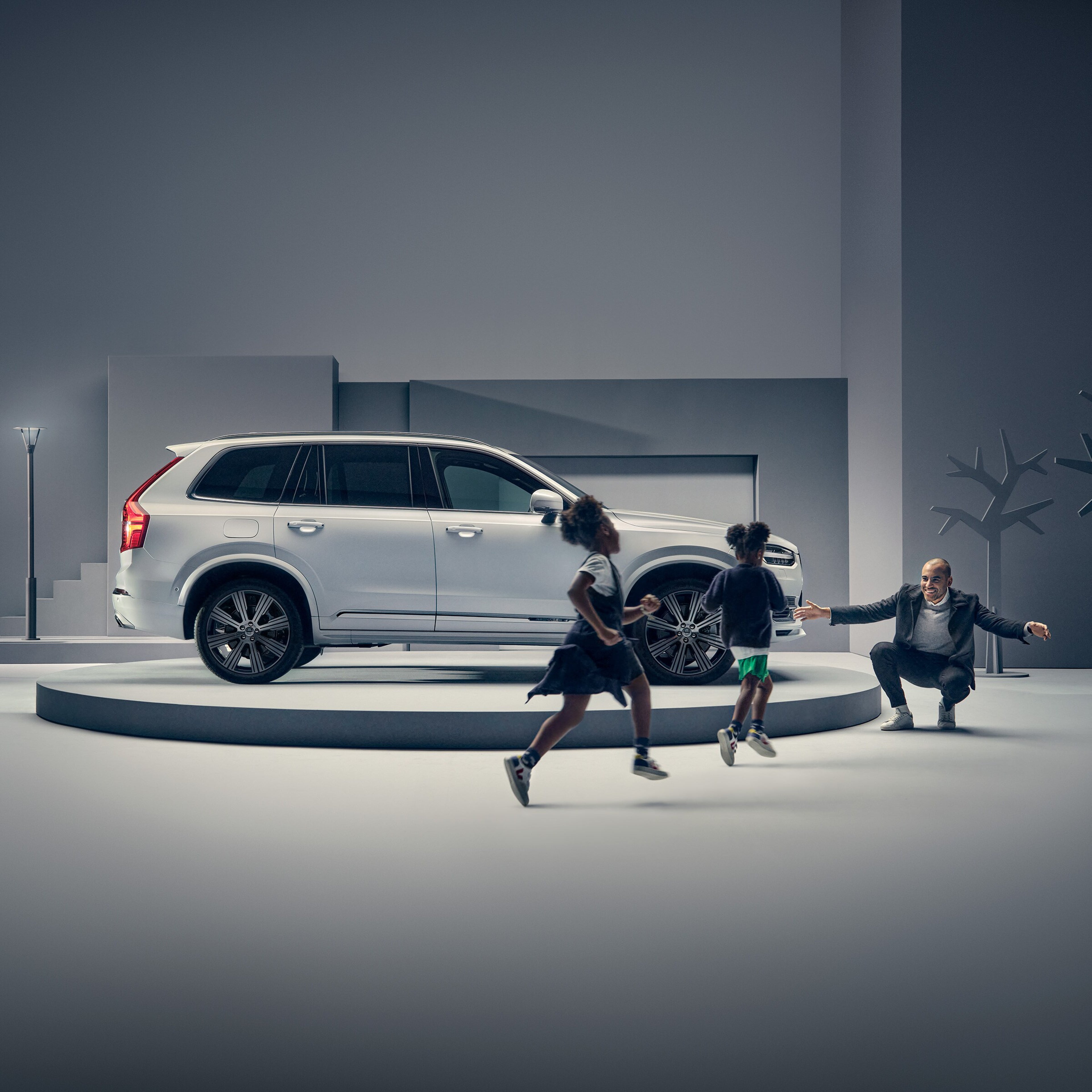 一名讲台上的男子在沃尔沃汽车前迎接两名孩子。