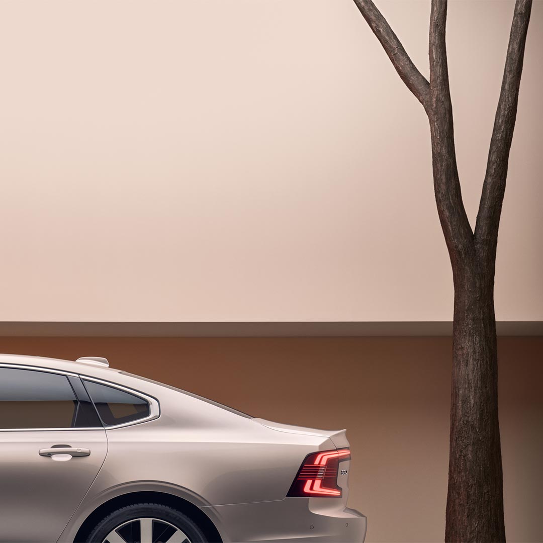 Volvo S90 插电式混合动力轿车停在树旁的图片。