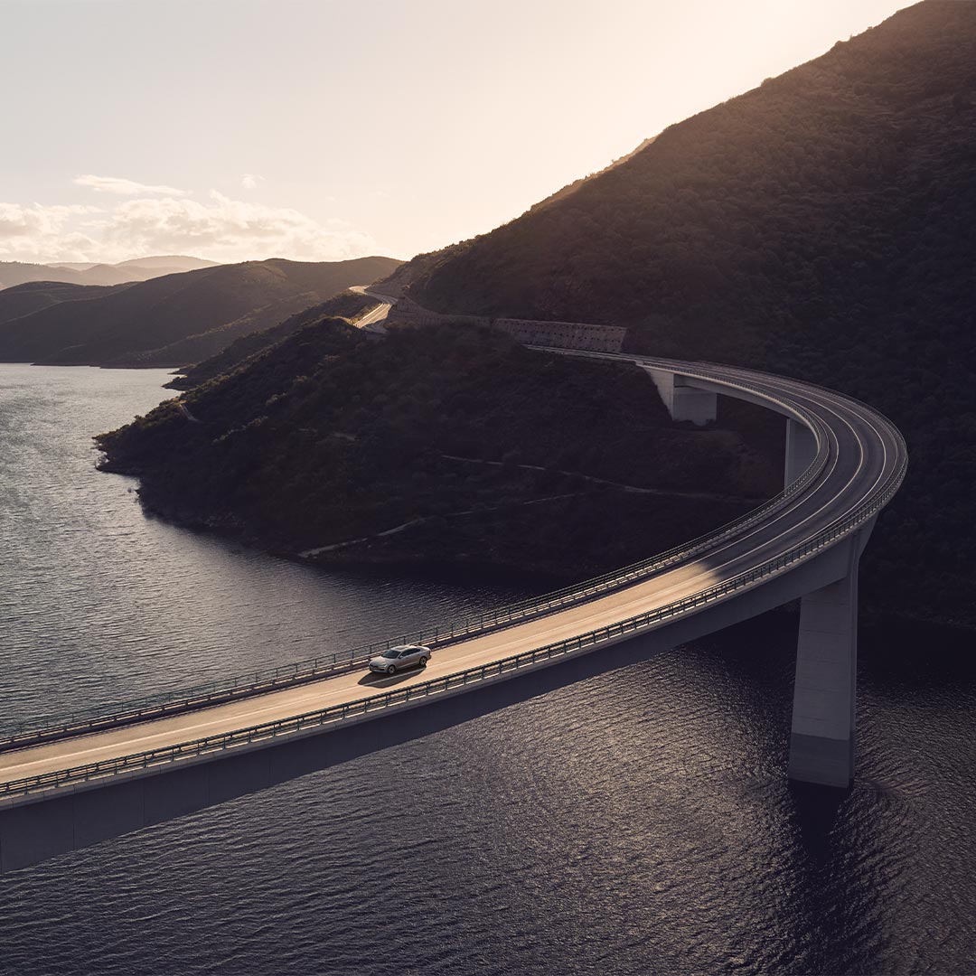 Volvo S90 插电式混合动力轿车驶过大桥，俯瞰河流山川的广角图片。