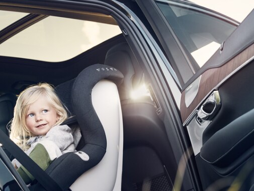 A rearward-facing child car seat with a young girl sitting in the back seat of a Volvo car.